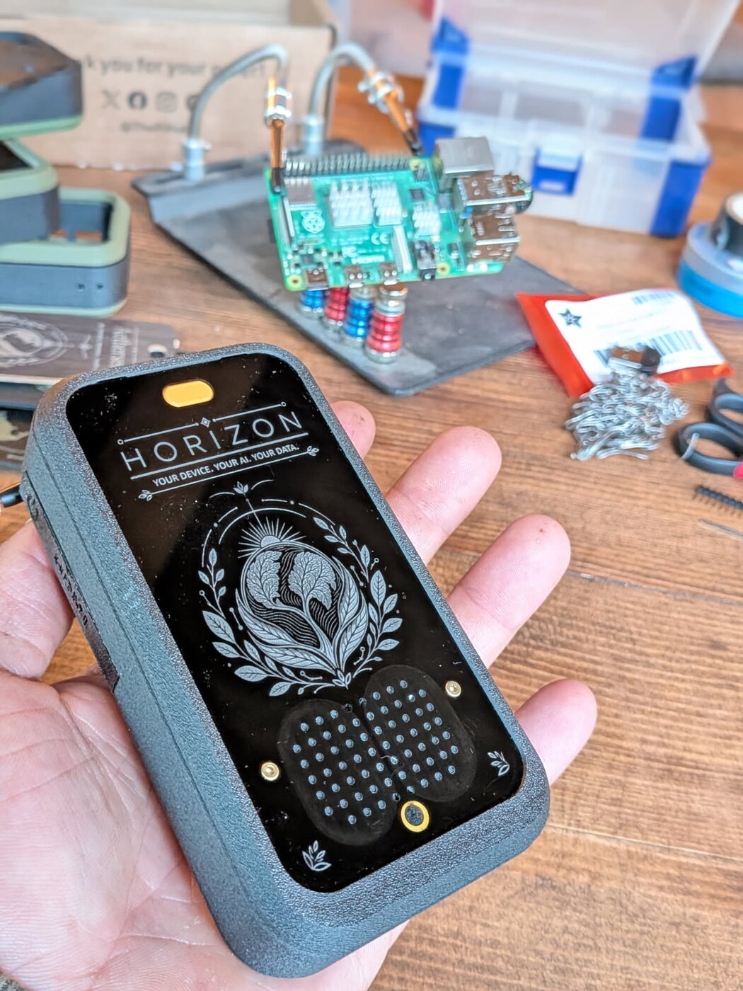 The real engraved Horizon prototype held in hand on a workbench, a Raspberry Pi on a soldering jig behind it. Engraving reads: Horizon — Your device. Your AI. Your data.